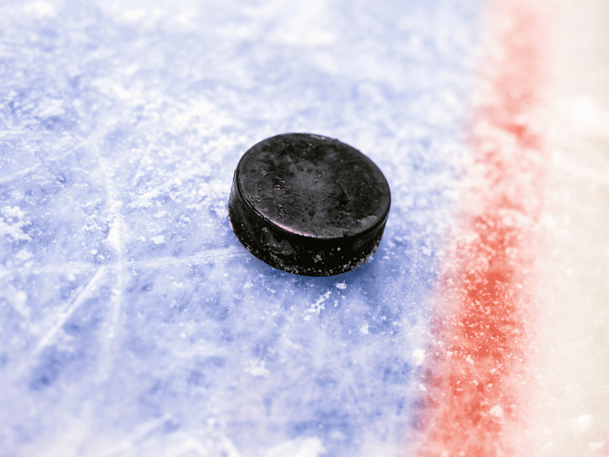 A Black Ice Hockey Puck Sits On Blue Ice Close To A Red Line On An Ice Hockey Rink