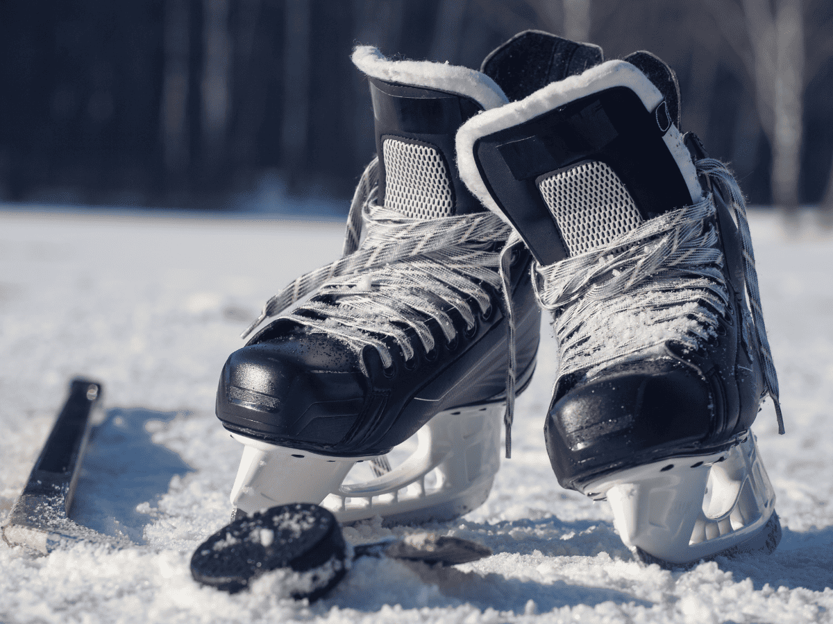 Black Ice Hockey Skates Lie On Snowy Ice With A Puck And A Hockey Stick